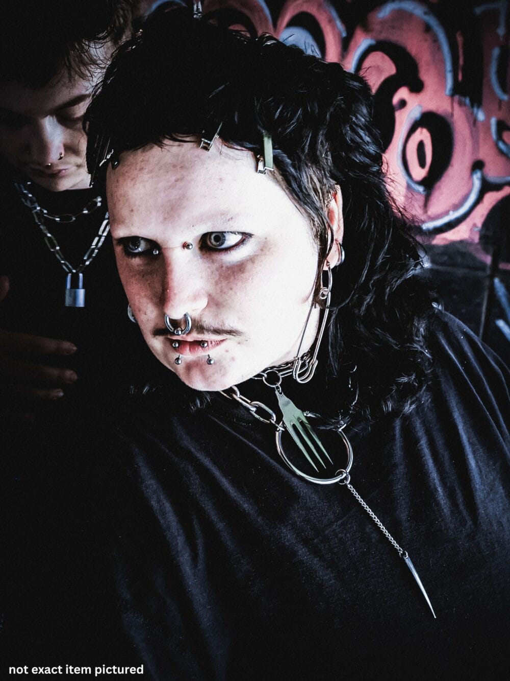 alternative styled person with piercings, black mullet haircut and cool stainless steel jewellery. image is from a brand photoshoot and has graffiti in the background.