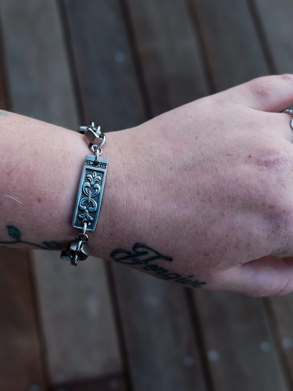 an image of a stainless steel bracelet on the wrist of someone with a wrist tattoo. the bracelet contains segments made from pieces of vintage stainless steel cutlery.