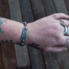 an image of a stainless steel bracelet on the wrist of someone with a wrist tattoo. the bracelet contains segments made from pieces of vintage stainless steel cutlery.