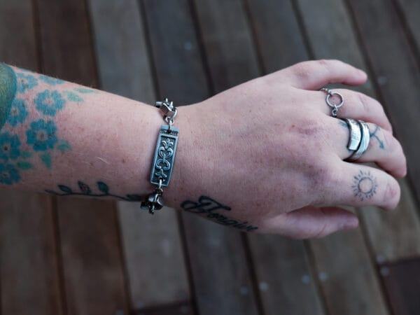 an image of a stainless steel bracelet on the wrist of someone with a wrist tattoo. the bracelet contains segments made from pieces of vintage stainless steel cutlery.