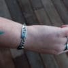 an image of a stainless steel bracelet on the wrist of someone with a wrist tattoo. the bracelet contains segments made from pieces of vintage stainless steel cutlery.