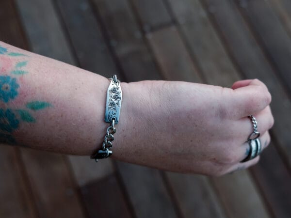 an image of a stainless steel bracelet on the wrist of someone with a wrist tattoo. the bracelet contains segments made from pieces of vintage stainless steel cutlery.