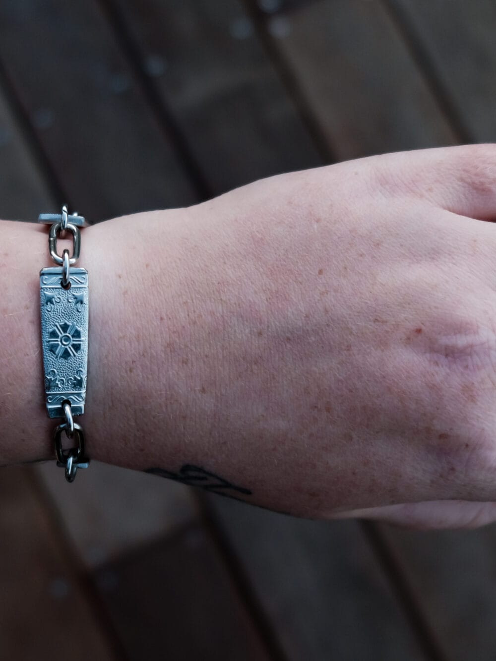 an image of a stainless steel bracelet on the wrist of someone with a wrist tattoo. the bracelet contains segments made from pieces of vintage stainless steel cutlery.