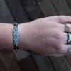 an image of a stainless steel bracelet on the wrist of someone with a wrist tattoo. the bracelet contains segments made from pieces of vintage stainless steel cutlery.