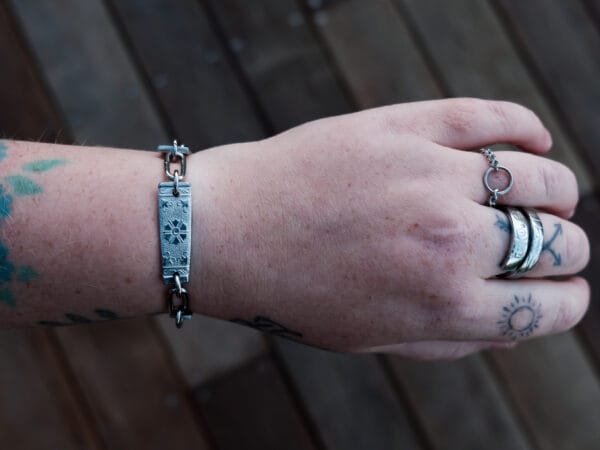 an image of a stainless steel bracelet on the wrist of someone with a wrist tattoo. the bracelet contains segments made from pieces of vintage stainless steel cutlery.