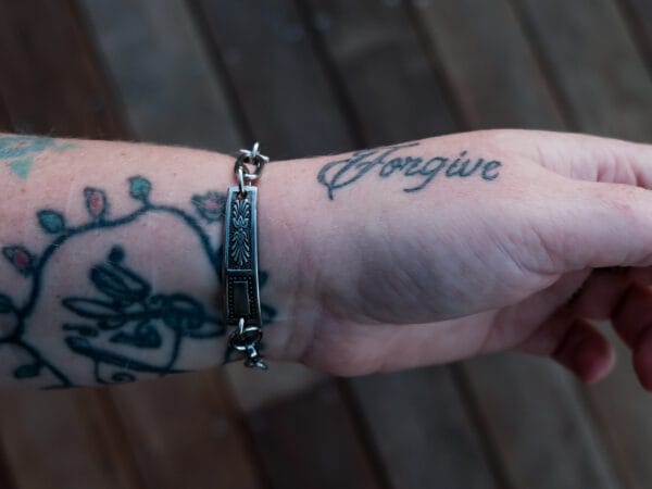an image of a stainless steel bracelet on the wrist of someone with a wrist tattoo. the bracelet contains segments made from pieces of vintage stainless steel cutlery.