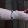 an image of a stainless steel bracelet on the wrist of someone with a wrist tattoo. the bracelet contains segments made from pieces of vintage stainless steel cutlery.