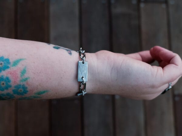 an image of a stainless steel bracelet on the wrist of someone with a wrist tattoo. the bracelet contains segments made from pieces of vintage stainless steel cutlery.