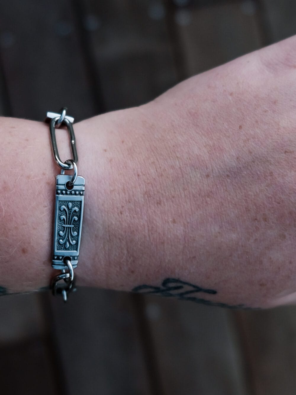 an image of a stainless steel bracelet on the wrist of someone with a wrist tattoo. the bracelet contains segments made from pieces of vintage stainless steel cutlery.