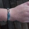 an image of a stainless steel bracelet on the wrist of someone with a wrist tattoo. the bracelet contains segments made from pieces of vintage stainless steel cutlery.