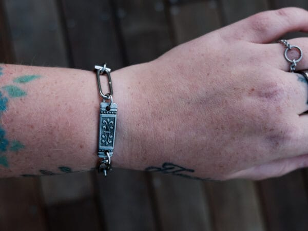 an image of a stainless steel bracelet on the wrist of someone with a wrist tattoo. the bracelet contains segments made from pieces of vintage stainless steel cutlery.