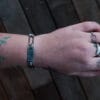 an image of a stainless steel bracelet on the wrist of someone with a wrist tattoo. the bracelet contains segments made from pieces of vintage stainless steel cutlery.