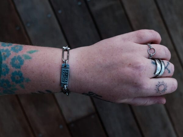 an image of a stainless steel bracelet on the wrist of someone with a wrist tattoo. the bracelet contains segments made from pieces of vintage stainless steel cutlery.