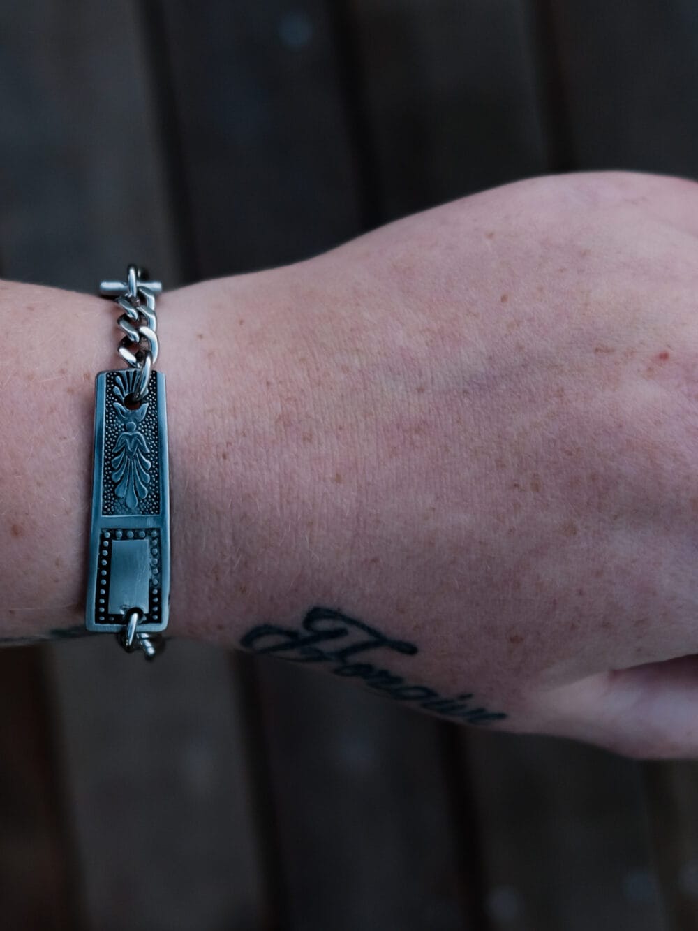 an image of a stainless steel bracelet on the wrist of someone with a wrist tattoo. the bracelet contains segments made from pieces of vintage stainless steel cutlery.
