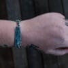 an image of a stainless steel bracelet on the wrist of someone with a wrist tattoo. the bracelet contains segments made from pieces of vintage stainless steel cutlery.