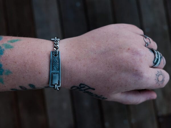 an image of a stainless steel bracelet on the wrist of someone with a wrist tattoo. the bracelet contains segments made from pieces of vintage stainless steel cutlery.