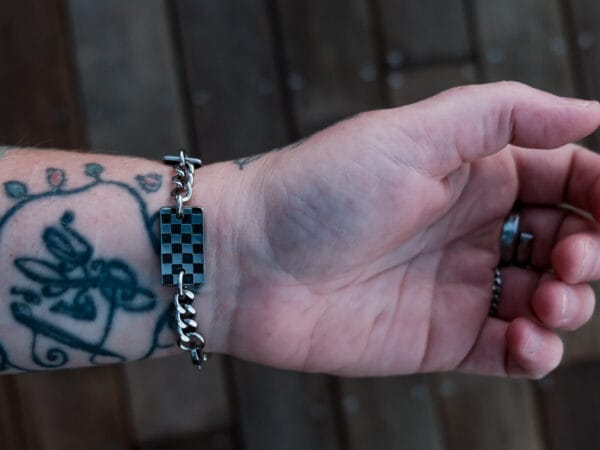 an image of a stainless steel bracelet on the wrist of someone with a wrist tattoo. the bracelet contains segments made from pieces of vintage stainless steel cutlery.