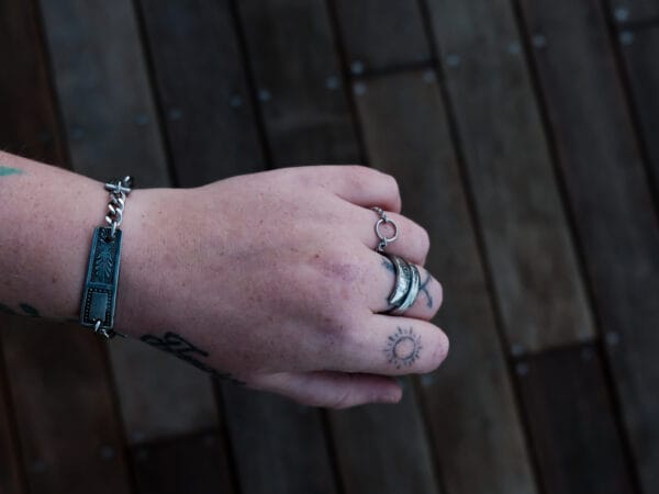 an image of a stainless steel bracelet on the wrist of someone with a wrist tattoo. the bracelet contains segments made from pieces of vintage stainless steel cutlery.
