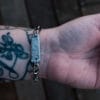 an image of a stainless steel bracelet on the wrist of someone with a wrist tattoo. the bracelet contains segments made from pieces of vintage stainless steel cutlery.