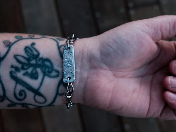 an image of a stainless steel bracelet on the wrist of someone with a wrist tattoo. the bracelet contains segments made from pieces of vintage stainless steel cutlery.