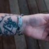 an image of a stainless steel bracelet on the wrist of someone with a wrist tattoo. the bracelet contains segments made from pieces of vintage stainless steel cutlery.
