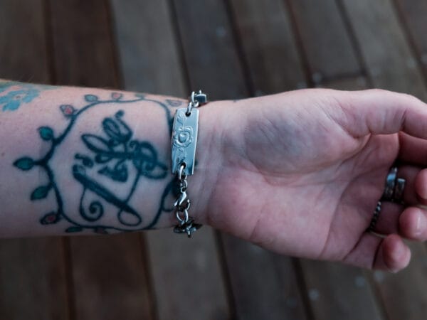 an image of a stainless steel bracelet on the wrist of someone with a wrist tattoo. the bracelet contains segments made from pieces of vintage stainless steel cutlery.
