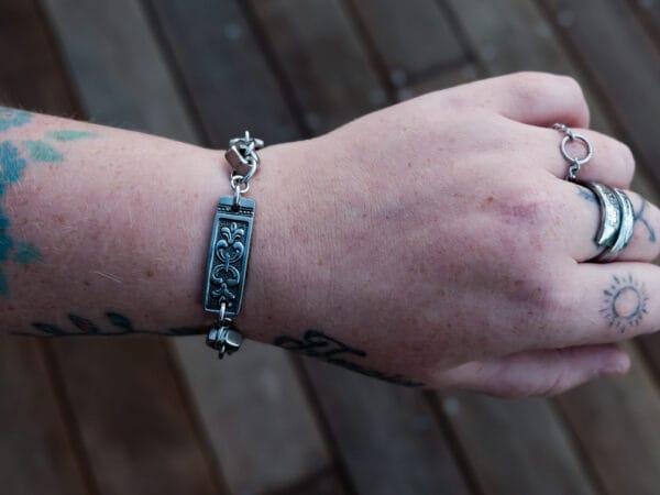 an image of a stainless steel bracelet on the wrist of someone with a wrist tattoo. the bracelet contains segments made from pieces of vintage stainless steel cutlery.