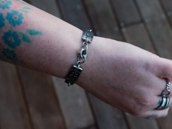 an image of a stainless steel bracelet on the wrist of someone with a wrist tattoo. the bracelet contains segments made from pieces of vintage stainless steel cutlery.