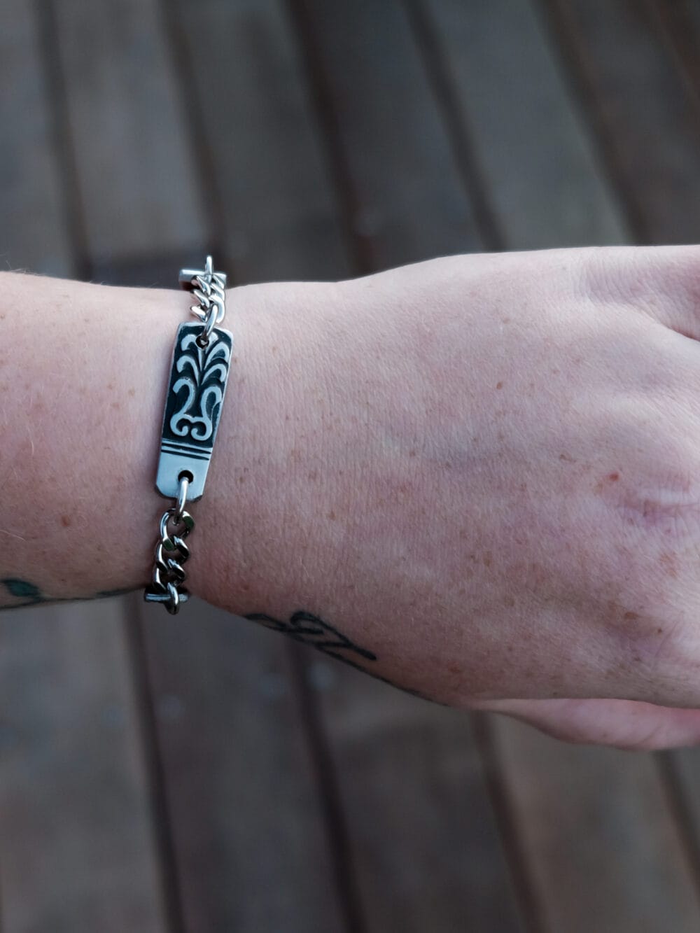 an image of a stainless steel bracelet on the wrist of someone with a wrist tattoo. the bracelet contains segments made from pieces of vintage stainless steel cutlery.