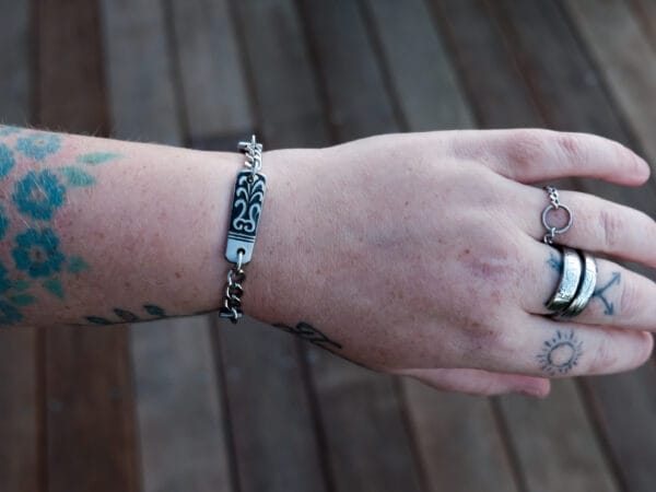 an image of a stainless steel bracelet on the wrist of someone with a wrist tattoo. the bracelet contains segments made from pieces of vintage stainless steel cutlery.