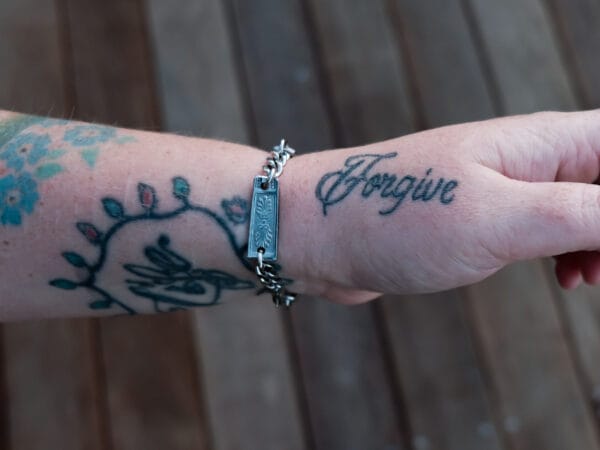 an image of a stainless steel bracelet on the wrist of someone with a wrist tattoo. the bracelet contains segments made from pieces of vintage stainless steel cutlery.