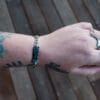 an image of a stainless steel bracelet on the wrist of someone with a wrist tattoo. the bracelet contains segments made from pieces of vintage stainless steel cutlery.