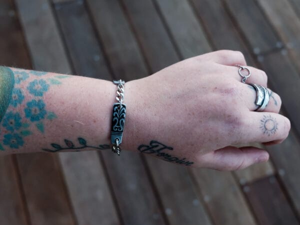an image of a stainless steel bracelet on the wrist of someone with a wrist tattoo. the bracelet contains segments made from pieces of vintage stainless steel cutlery.