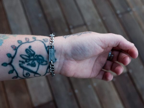 an image of a stainless steel bracelet on the wrist of someone with a wrist tattoo. the bracelet contains segments made from pieces of vintage stainless steel cutlery.