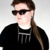 a woman wearing sunglasses, a black shirt and a stainless steel necklace made from the handle and fork tines of a vintage fork.