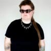 a woman with sunglasses and a black shirt wearing a necklace made from chunky stainless steel chain and hex nuts as charms along it.
