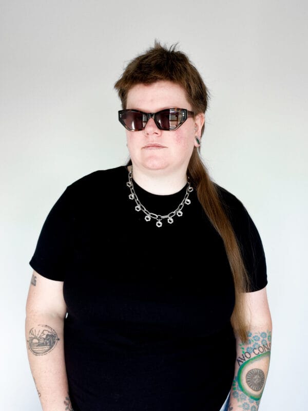 a woman with sunglasses and a black shirt wearing a necklace made from chunky stainless steel chain and hex nuts as charms along it.