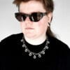 a woman with sunglasses and a black shirt wearing a necklace made from chunky stainless steel chain and hex nuts as charms along it.