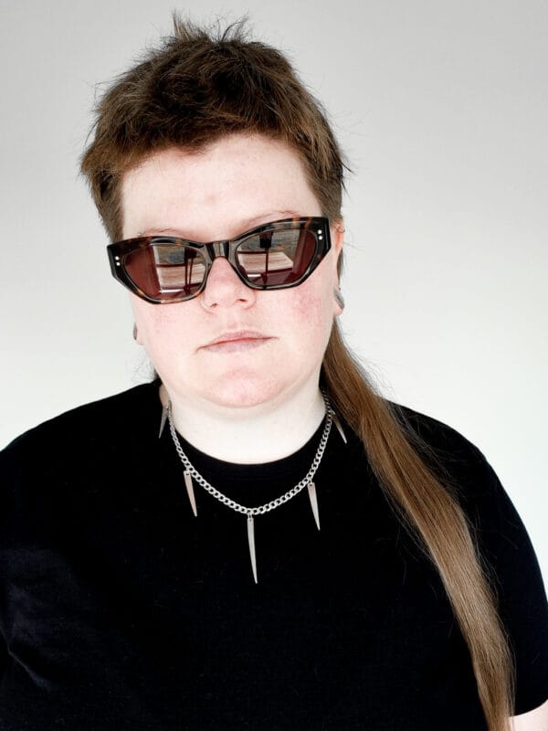 a woman with sunglasses and a black shirt on wearing a stainless steel curb chain necklace with fork tines as charms for a product photoshoot