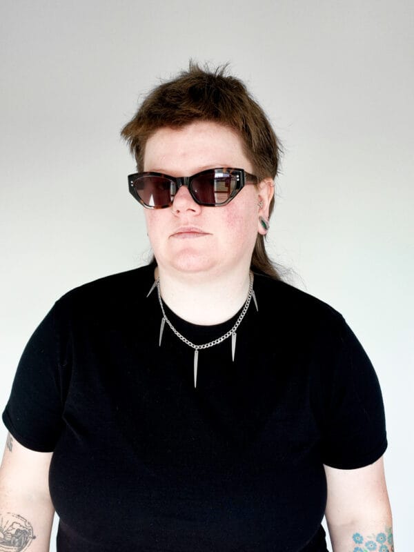 a woman with sunglasses and a black shirt on wearing a stainless steel curb chain necklace with fork tines as charms for a product photoshoot