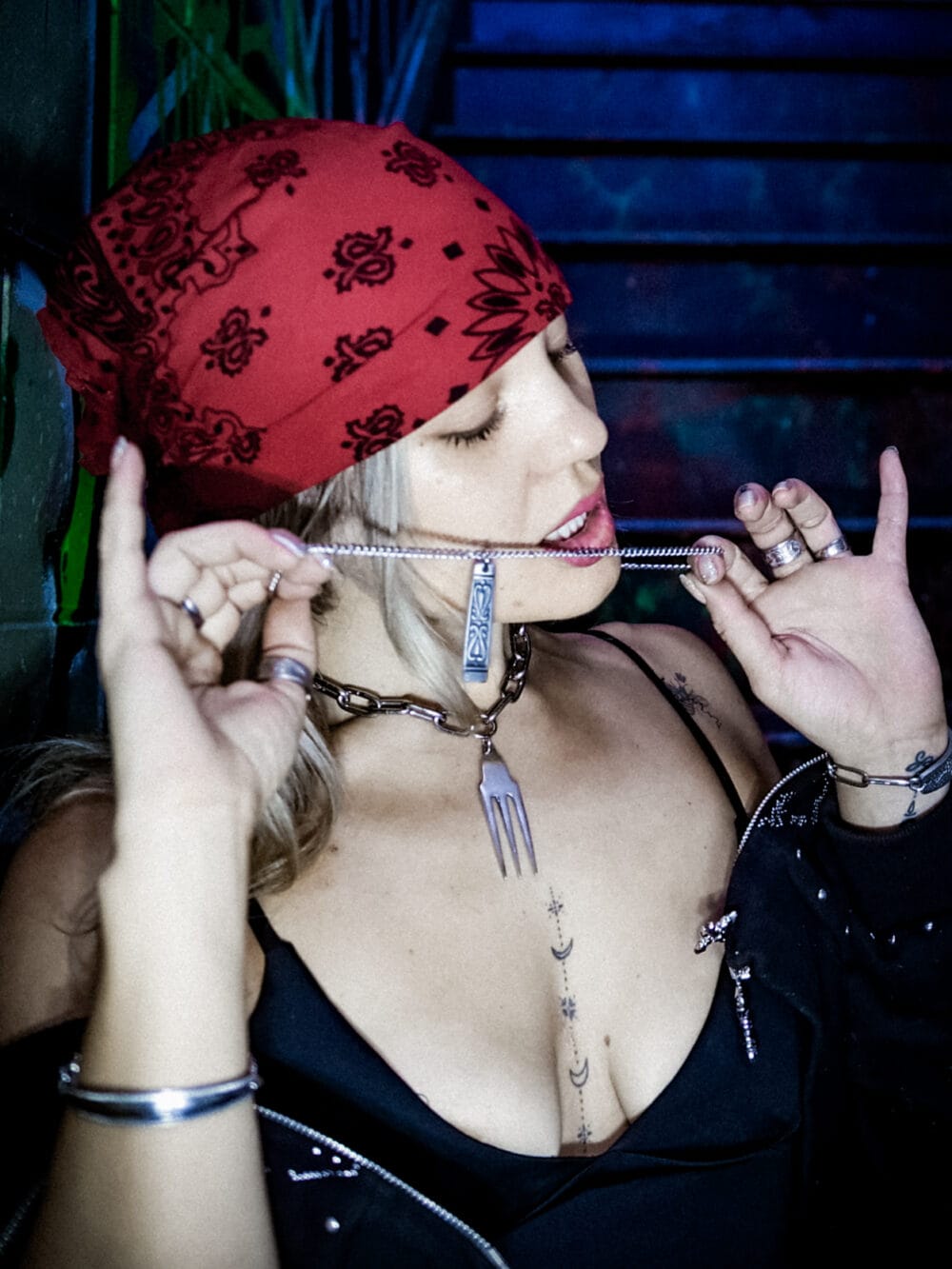 a woman with a red bandana and single top with tattoos wearing a stainless steel pendant made from a thrifted fork placed on a small black cushion for a product photoshoot