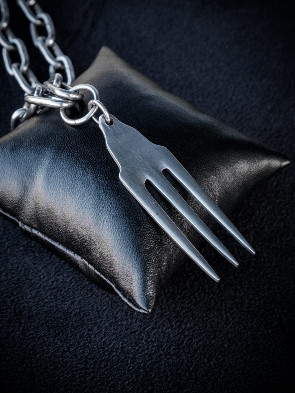 a stainless steel pendant made from a thrifted fork placed on a small black cushion for a product photoshoot