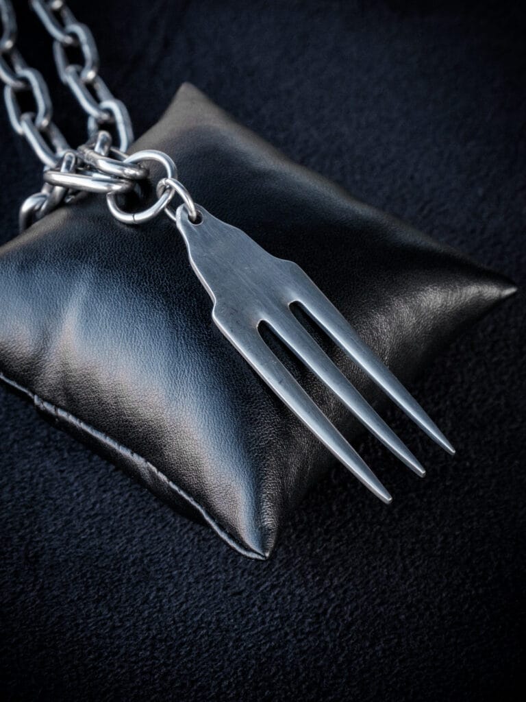 a stainless steel pendant made from a thrifted fork placed on a small black cushion for a product photoshoot