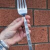 an image of a hand holding a giant vintage fork. the handles have a flower and swirly leaf pattern