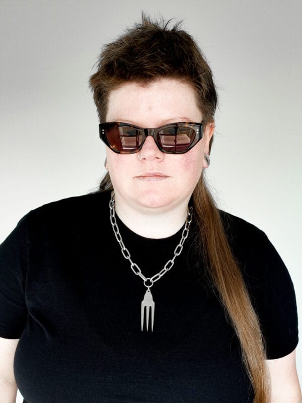 a woman with sunglasses and a black shirt wearing a stainless steel pendant made from a thrifted fork placed on a small black cushion for a product photoshoot