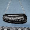 a product photo of a black faux leather handbag with spikes and chains.