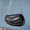 a product photo of a black faux leather handbag with spikes and chains.