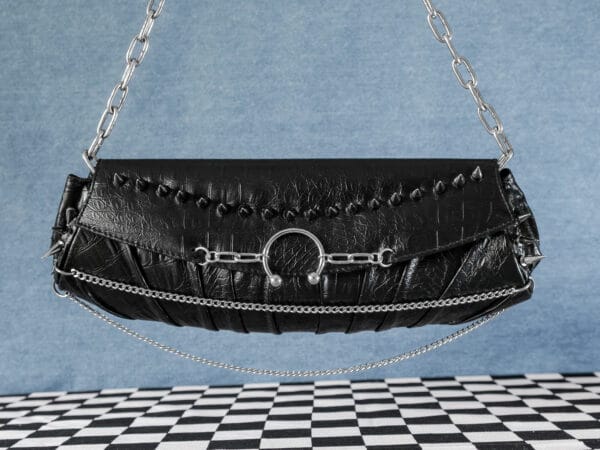 a product photo of a black faux leather handbag with spikes and chains.