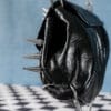 a product photo of a black faux leather handbag with spikes and chains.