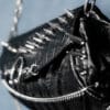 a product photo of a black faux leather handbag with spikes and chains.